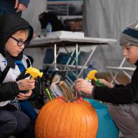 two boys hammer nails into a pumpkin